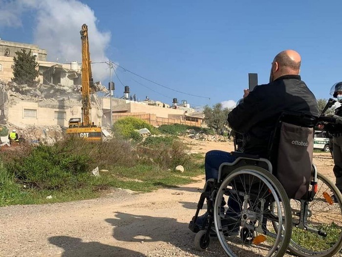 Ein Mann im Rollstuhl shaut, wie die israelische Maschinen sein Haus zerstören